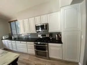 White refinished kitchen cabinets with stainless steel appliances and dark countertops